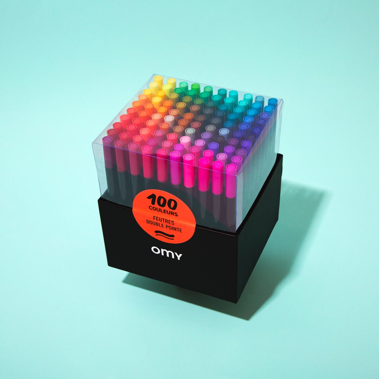 OMY Set of 100 colorful markers in a clear holder on a light blue background