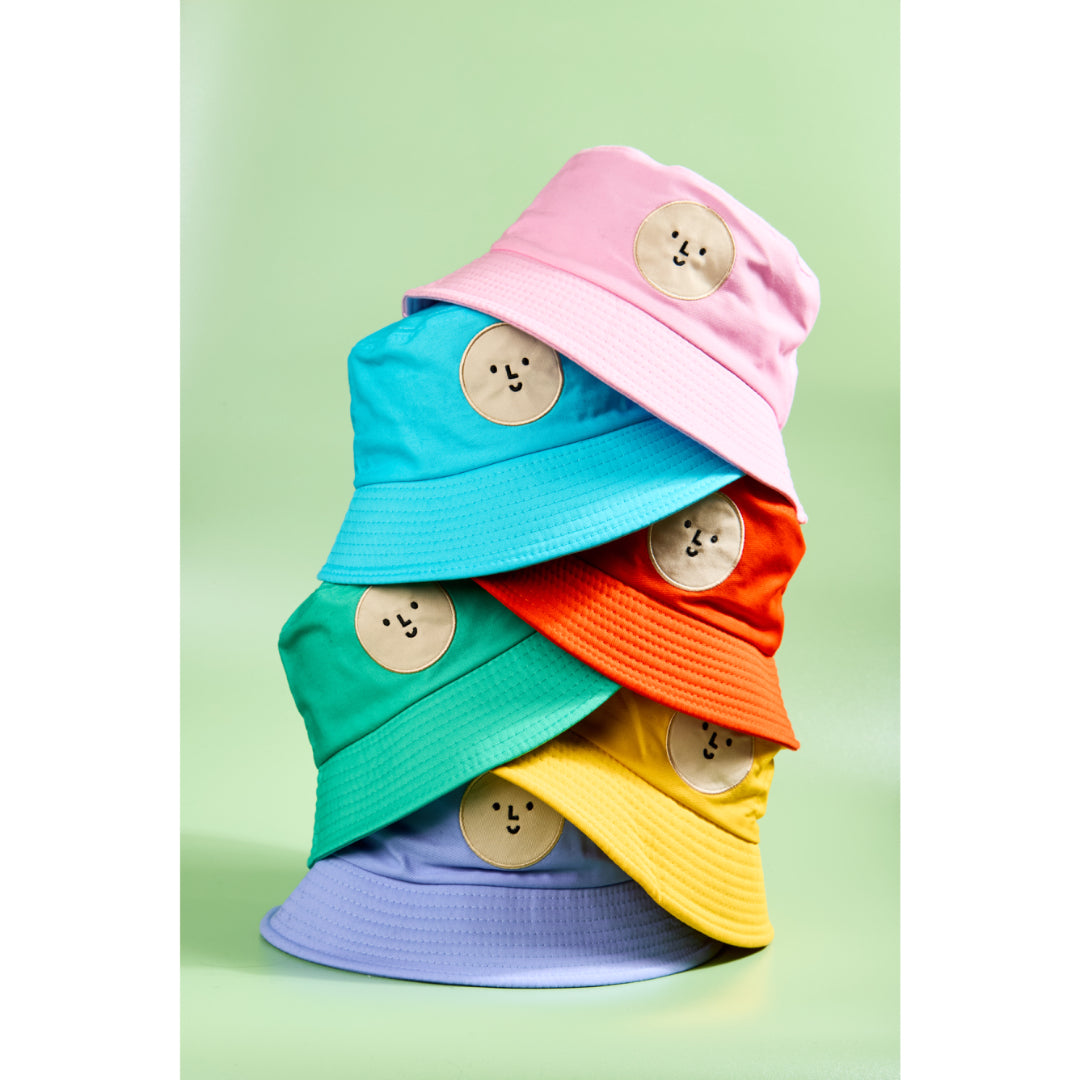 Stack of colorful bucket hats with smiley face buttons on a light green background