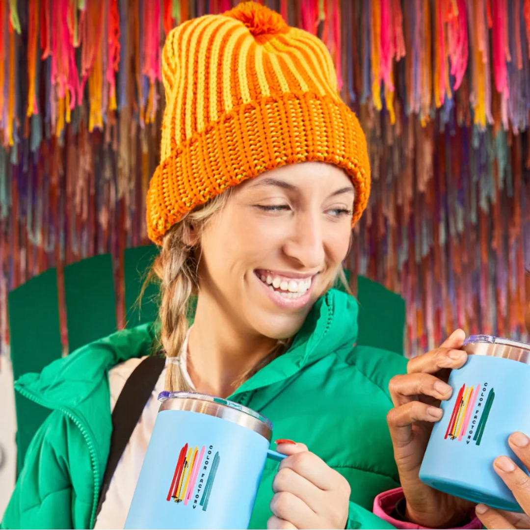 Woman in chunky knit beanie with yellow and orange contrasting stripes and fluffy pom pom on top.