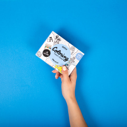 Hand holding a card with 'omy' branded Coloring book against a blue background
