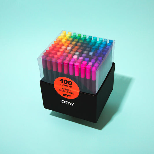 OMY Set of 100 colorful markers in a clear holder on a light blue background