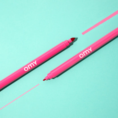 Two pink markers with 'omy' branding on a light blue background