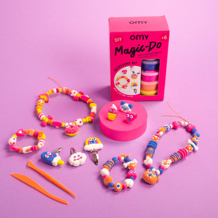 Colorful jewelry-making kit with 'OMY' packaging on a pink background