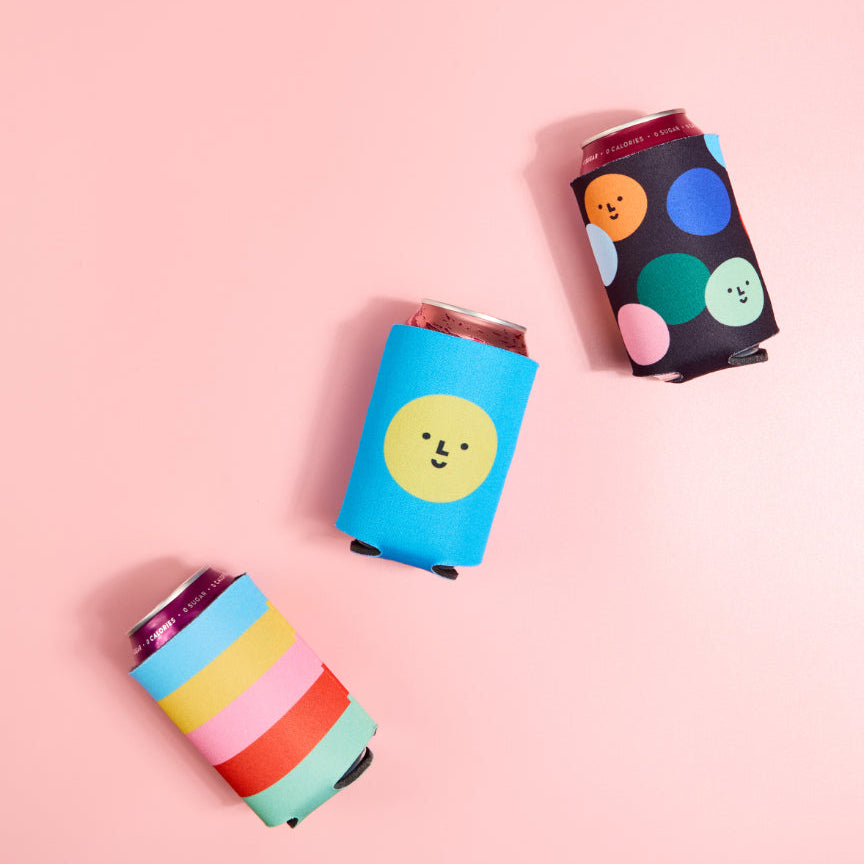 Three colorful can coolers with different designs on a pink background