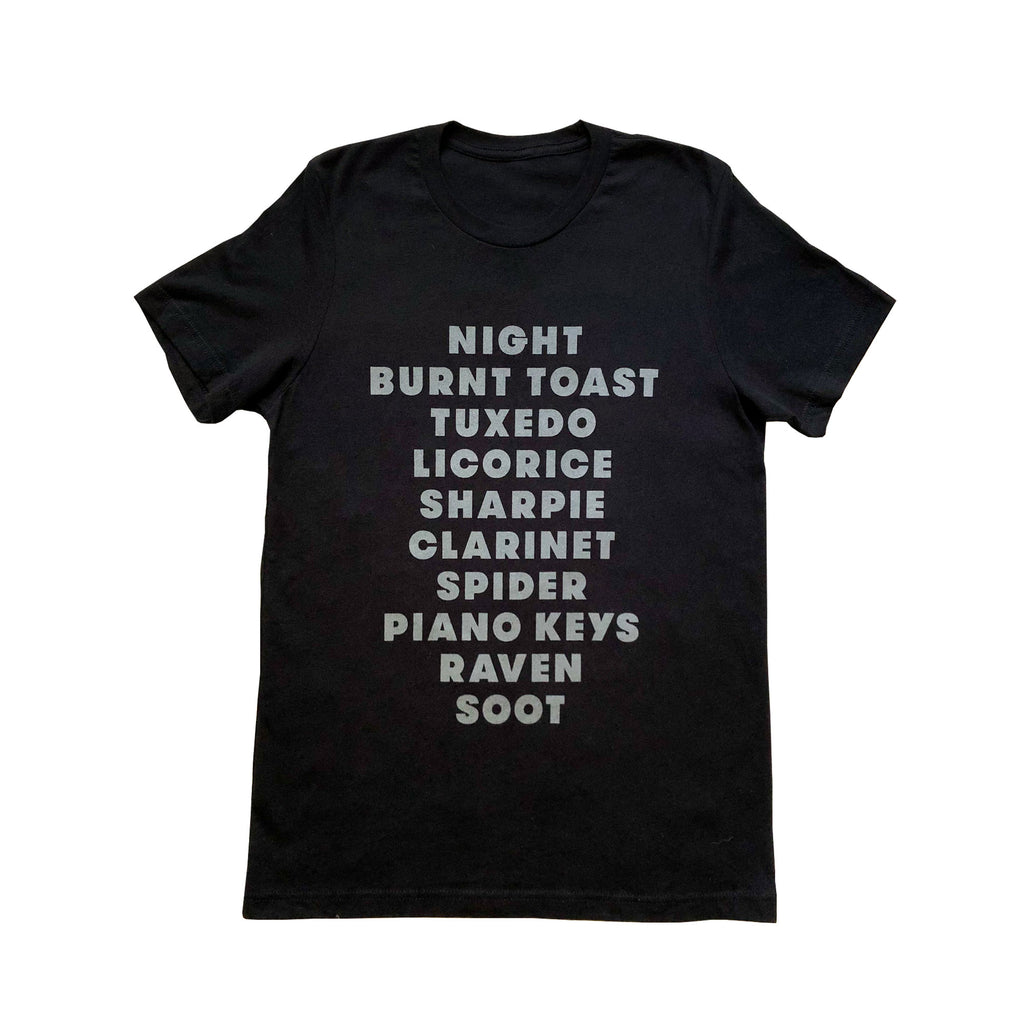 A  black, adult t-shirt with a list of "black" items printed on the front (in light gray ink). List includes happy items (like licorice) as well as funny items (like sharpie or soot.